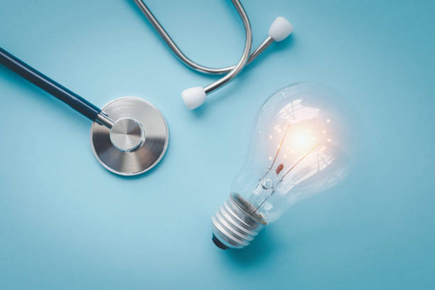 Doctor’s medical Stethoscope, laid face-down on a table, processed in blue hues. Flat lay heart monitor, medical stethoscope and light bulb on blue background.