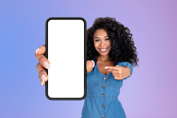 istock African woman pointing at big phone with empty screen, purple background 1455275983