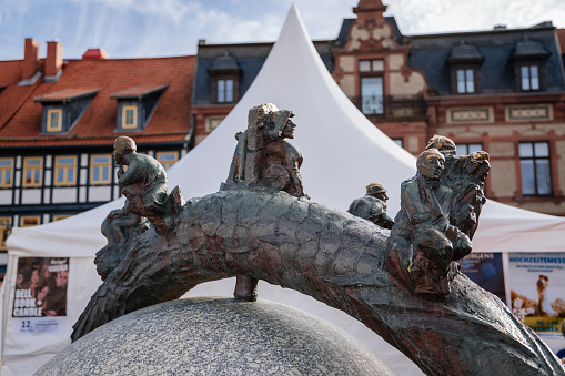 Wernigerode, Saxony-Anhalt, Germany, 29 October 2022:  Water fountain in the form of ball with tree trunk and sculptures sitting on it, Modern sculpture on streets of city, vintage timber frame houses