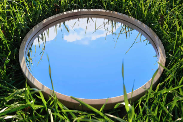 istock Cloudy Blue Sky Reflection in Round Wood Mirror on Summer Field with Green Grass. Nature Concept. Earth Day. Save Environment. Peace. Ecology Protection. Climate Change, Global Warming Effect Problem 1455277719