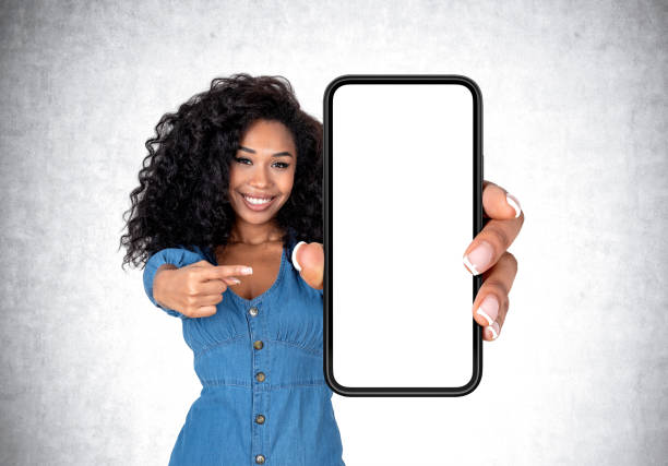 istock African woman pointing at big phone with blank screen, grey background 1455278024