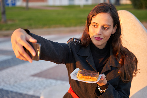 Woman taking a selfie while eating a chocolate waffle at sunset