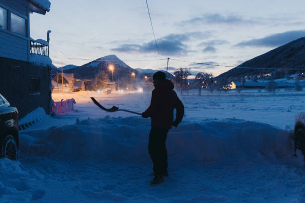 Active man in red jacket shoveling the snow in the rural place near the car in Scandinavia
