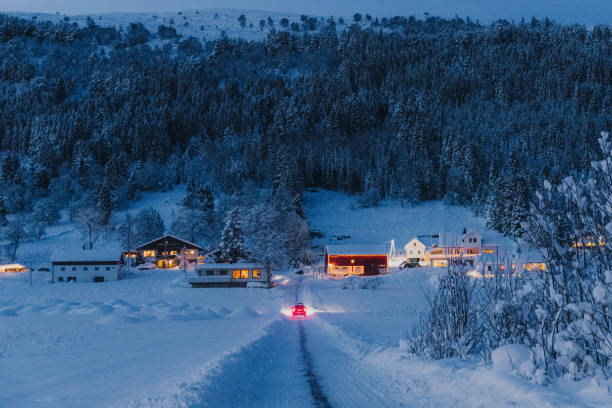 Scenic view of a car driving up the hill to the beautiful village in Christmas lights and decoration with view of the snowcapped mountain in Norway, Scandinavia