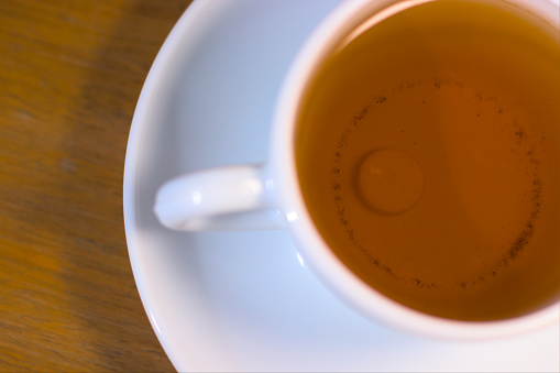 Cup of tea with pill inside on a wooden table.