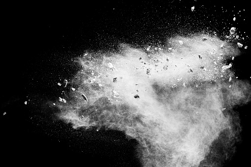 White powder with small stones on black background. Small granite rock stone fly on dust against dark background.