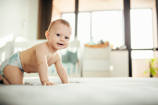 Adorable little baby boy crawling on bed.