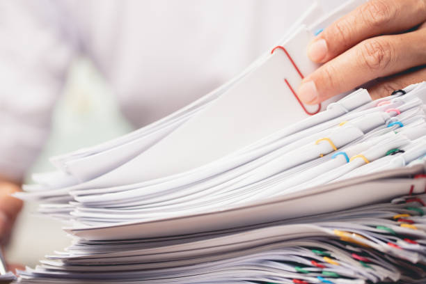 istock Hands of a man in a white shirt searching for contract agreement documents in Stack of Group report papers clipped in color clips. 1455285906