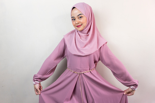 Hermosa mujer asiática sonriente con hijab rosa levanta la falda y luce segura aislada sobre fondo gris photo
