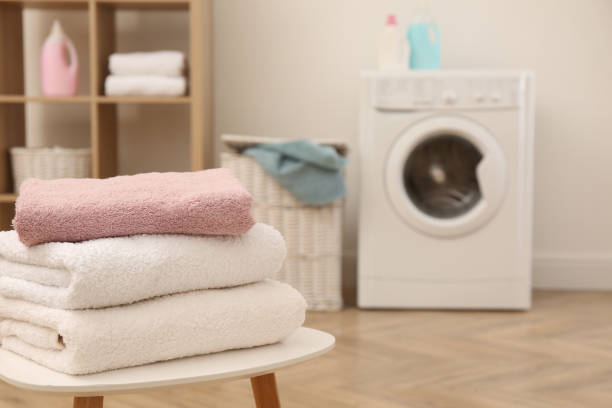 istock Stack of clean terry towels on white table in laundry room. Space for text 1455286462