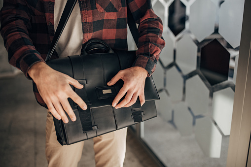 One man, unrecognizable male opening a modern leather bag.