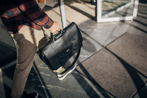 One man, unrecognizable male carrying a modern leather bag.