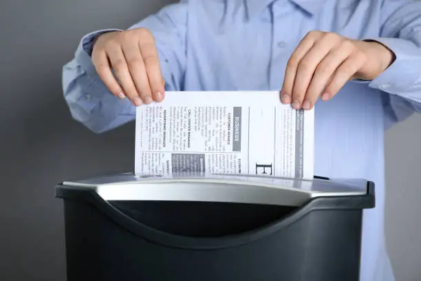 Woman destroying newspaper with shredder on grey background, closeup