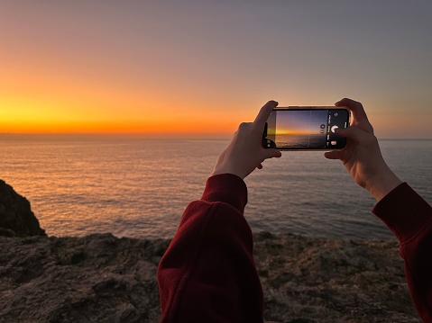 Hands holding a mobile phone taking a picture of the sunset