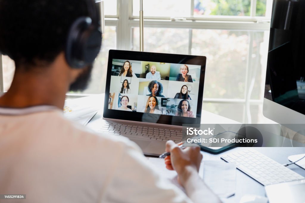 Over-the-shoulder view unrecognizable male college student attending online class An over-the-shoulder view of an unrecognizable university student meeting online with his teacher and fellow students. E-Learning Stock Photo