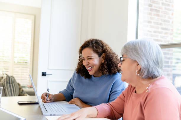 starsza mama i dorosła córka śmieją się podczas pracy nad budżetem - smart phone writing assistance business zdjęcia i obrazy z banku zdjęć