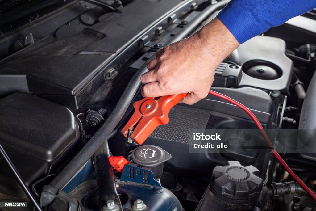 Mechanic is connecting a booster-cable to the battery in order to jump-start a car Assistance Stock Photo