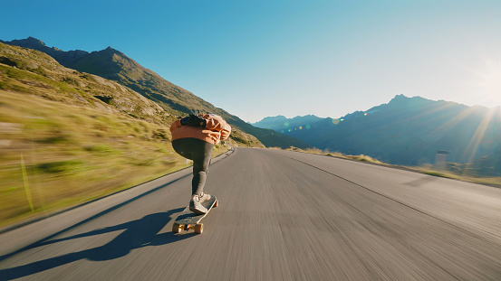 Cinematic downhill longboard session. Young woman skateboarding and making tricks between the curves on a mountain pass. Concept about extreme sports and people