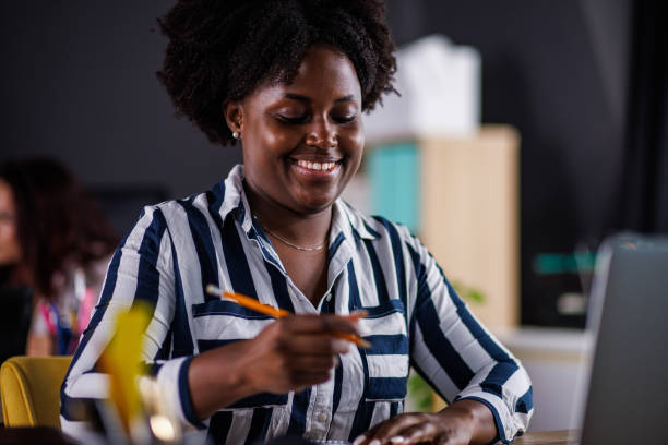 istock Charming Black businesswoman writing notes and using laptop when working at her desk 1455296217