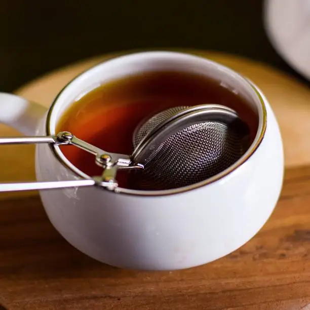 A closeup of a tea infuser in a cup of black tea.