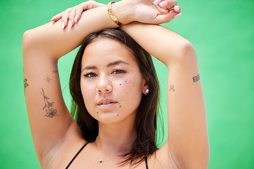 Face, beauty and tattoos with a model woman in studio on a green background with ink on her skin. Portrait, body art and natural with an attractive young female posing for edgy or trendy style