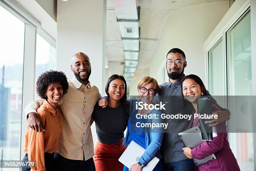 istock Smiling businesspeople standing arm in arm in an office hall 1455296779