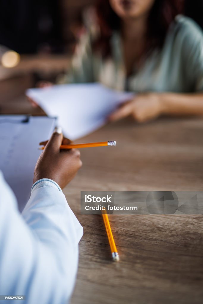 Woman holding a clipboard and writing notes while interviewing a candidate for a job Close up shot of unrecognizable businesswoman sitting at her desk, holding a clipboard and writing notes while interviewing a candidate for a job. Writing - Activity Stock Photo