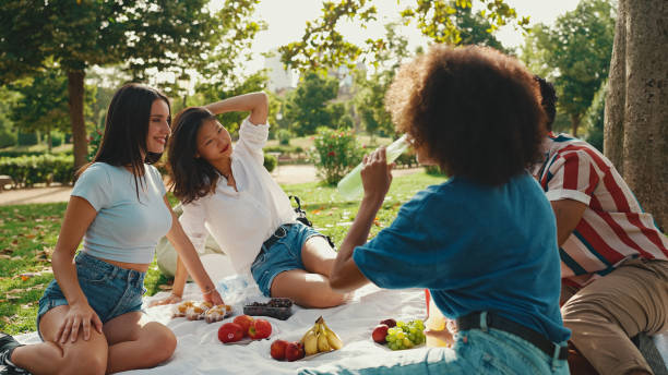 istock Happy smiling young multinational people at picnic on summer day outdoors. Friends have fun weekend together, relaxing in the park at picnic 1455298421