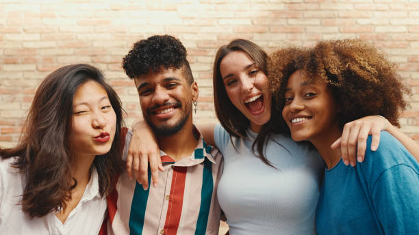 istock Happy, lovely multiethnic young people posing for the camera on summer day outdoors. Group of friends hugging tightly smiling at camera while standing on brick wall background 1455298459