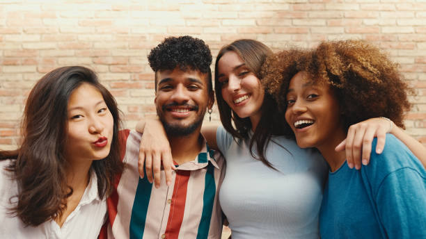 istock Happy, lovely multiethnic young people posing for the camera on summer day outdoors. Group of friends hugging tightly smiling at camera while standing on brick wall background 1455298465