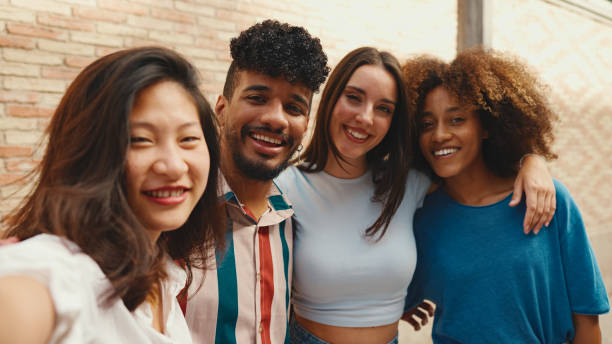 istock Happy, lovely multiethnic young people posing for the camera on summer day outdoors. Group of friends hugging tightly smiling at camera while standing on brick wall background 1455298496