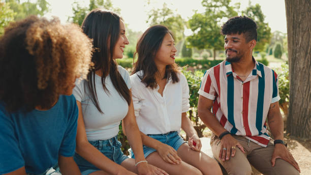 istock Happy multiethnic young people talking while sitting on park bench on summer day outdoors. Group of friends talking and laughing merrily in city park 1455298680