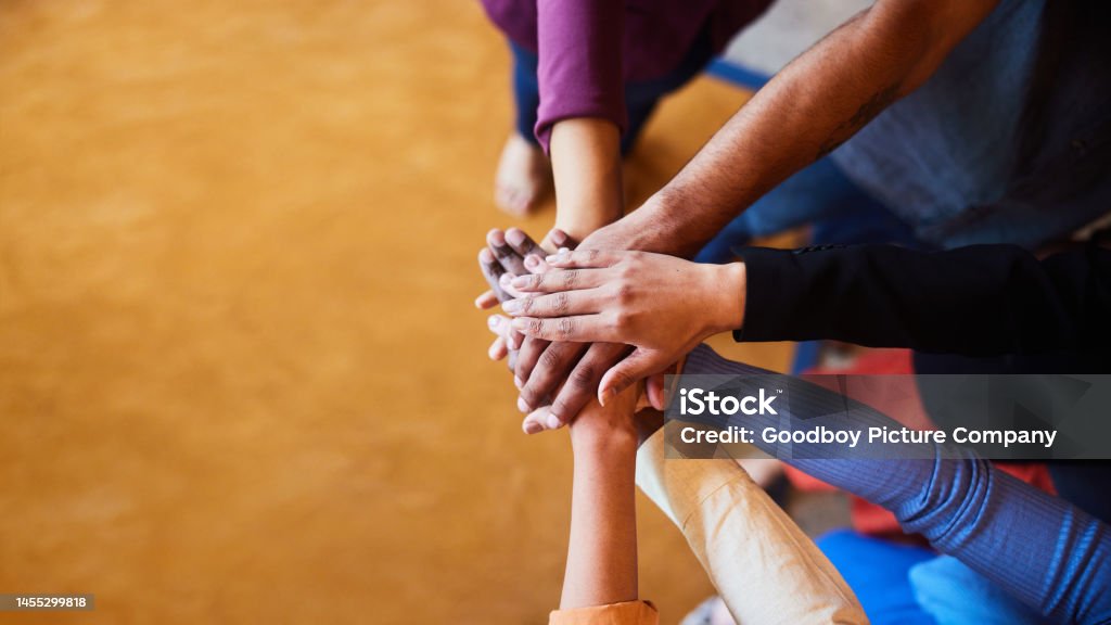 Diverse businesspeople standing with their hands together in an office High angle view of a group of diverse businesspeople standing in a semi circle with their hands in a pile in an office Teamwork Stock Photo