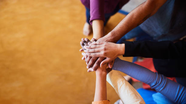 Diverse businesspeople standing with their hands together in an office High angle view of a group of diverse businesspeople standing in a semi circle with their hands in a pile in an office synergy series stock pictures, royalty-free photos & images