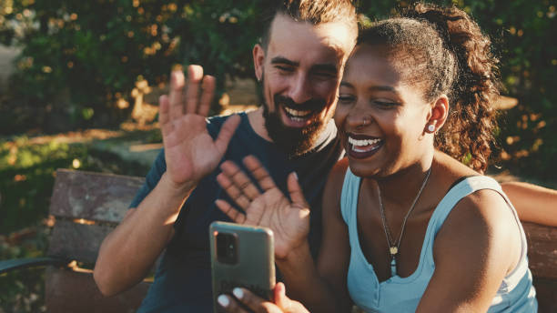 istock Happy smiling interracial couple taking selfie on phone while sitting on park bench. 1455300037