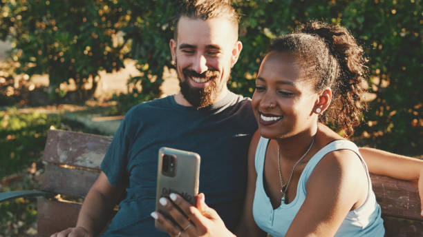 istock Happy smiling interracial couple taking selfie on phone while sitting on park bench. 1455300040