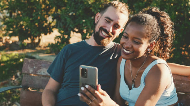 istock Happy smiling interracial couple taking selfie on phone while sitting on park bench. 1455300225