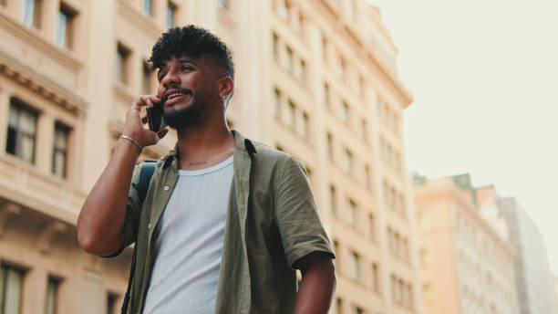 istock Young happy man with beard dressed in an olive-colored shirt is talking on cellphone standing on the old city background 1455300333