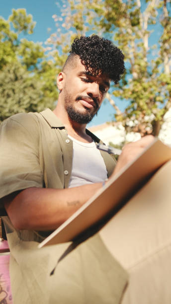 istock Young male student wearing an olive colored shirt takes notes in notepad while sitting on bench outside the university 1455300471