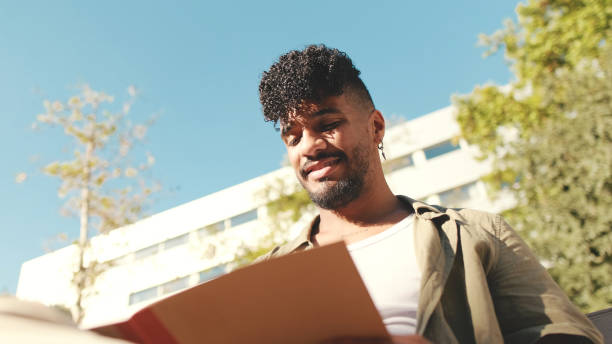 istock Young male student wearing an olive colored shirt takes notes in notepad while sitting on bench outside the university 1455300529