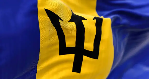Barbados national flag waving.Blue and yellow flag with a black Triton in the center. Rippled Fabric. Textured background. Selective focus. Realistic 3d illustration