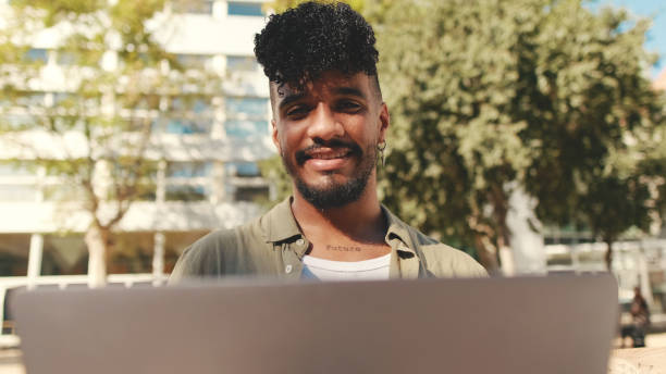 istock Close up, young male student wearing an olive colored shirt is working on pc laptop while sitting on bench outside the university 1455300580