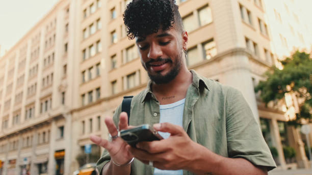 istock Young smiling man with beard dressed in an olive color shirt uses phone map app on the old city background 1455300621