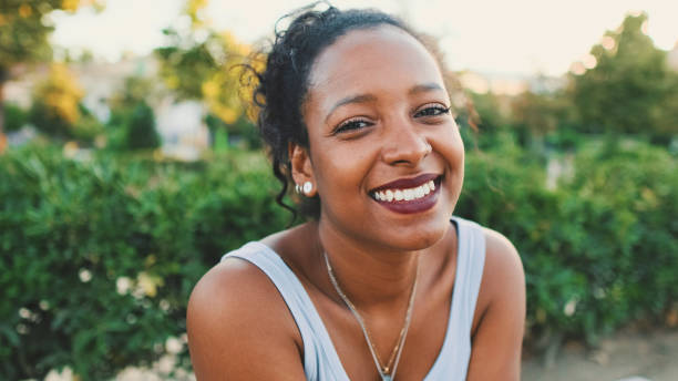 istock Young mixed race woman sitting on park bench, smiling, looking around 1455300907