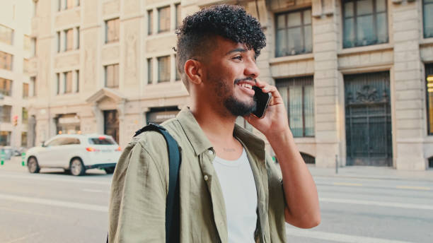 istock Young happy man with beard dressed in an olive-colored shirt is talking on cellphone standing on the old city background 1455301143