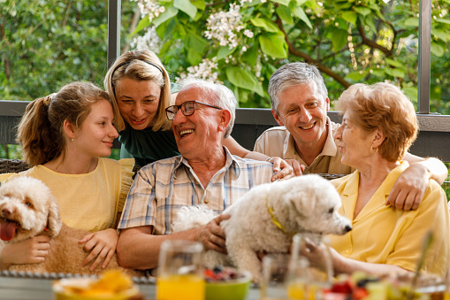 Portrait of happy three generation family and their dog cuddling and bonding during a celebratory party on the balcony.