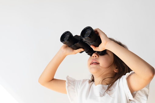 Little girl  is using binoculars in front of white background.