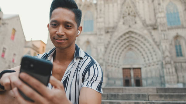istock Young man tourist on steps uses mobile phone while sitting on landmarks background 1455303075