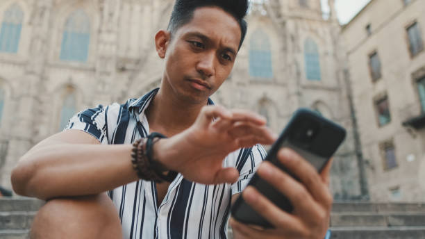 istock Young man tourist on steps uses mobile phone while sitting on landmarks background 1455303289