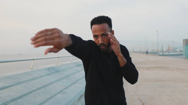 istock Young bearded male athlete boxer practicing punching technique while standing on the embankment 1455304364